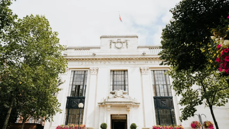 The white neo-classical facade of Islington Town Hall framed by lush green trees.