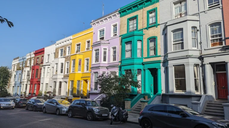 A wide shot of a residential street featuring a long row of colorful Victorian terraced houses with cars parked in front.