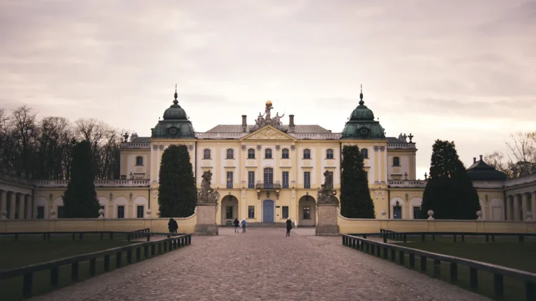 A grand view of a yellow baroque palace with green-domed towers and a central gravel path, illustrating the royal venue for the 2026 Bauska Festival.
