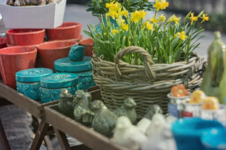 Yellow daffodils in a wicker basket among colorful ceramic pots and small decorative bird figurines.