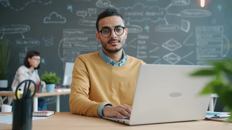A young professional man working on a laptop in a modern office setting.