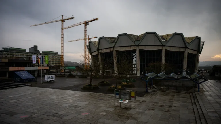 Multiple large construction cranes tower over a modern building site under a cloudy sky.