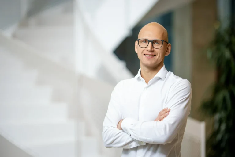 Smiling bald man wearing glasses and a white dress shirt standing with his arms crossed.