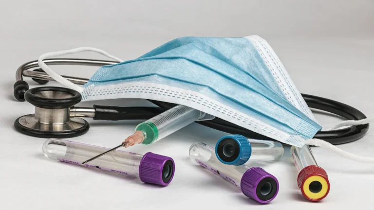 A medical stethoscope, protective face mask, and several test tubes used for routine student health screenings.