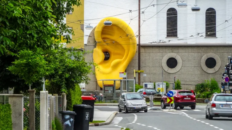 A giant yellow ear sculpture mounted onto the facade of a traditional white building.