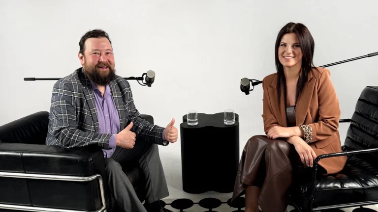 A man and woman sit in leather chairs for a podcast recording in a studio.