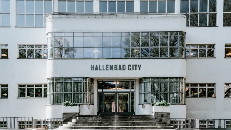 Facade of a historic white public swimming bath building featuring large windows and modernist architecture.