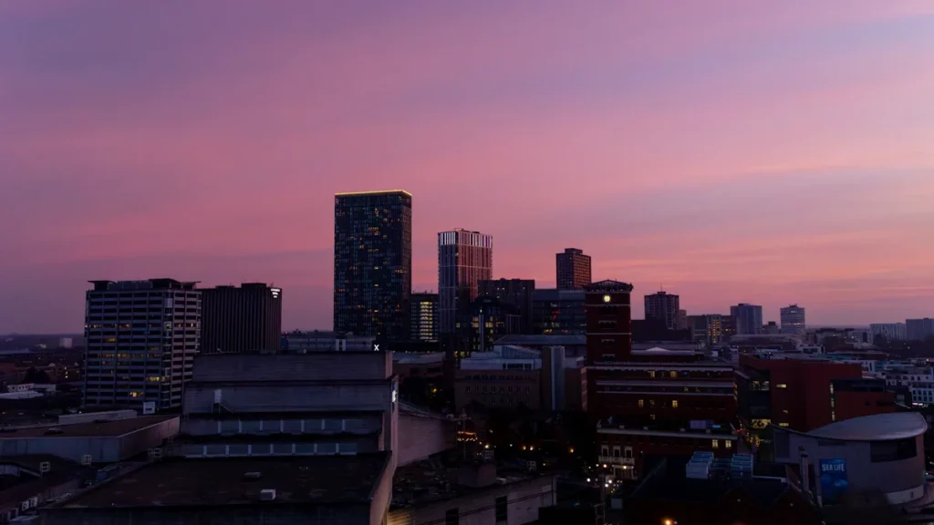 The Birmingham city skyline at dusk with a vibrant purple and red sky over modern skyscrapers.