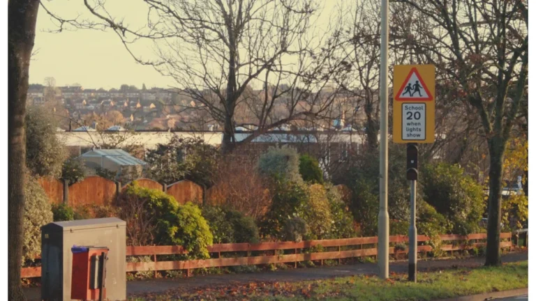 A yellow UK road sign indicating a 20 mph speed limit near a school neighborhood.