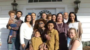 A large, diverse multi-generational family group smiling together in front of a white house.