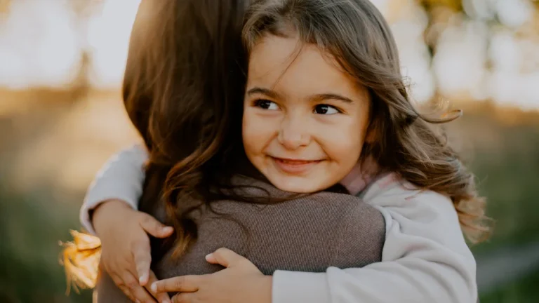 A smiling young girl receives a supportive hug from her foster carer.
