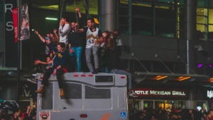 Fans celebrate on top of a bus during a victory parade at night.