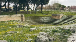A wide view of an ancient circular stone assembly place surrounded by grass and trees.