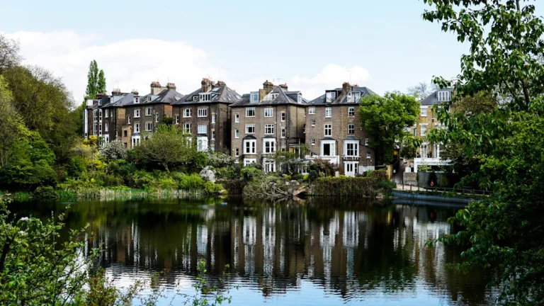 Traditional brown brick houses overlooking a serene pond surrounded by lush greenery in Hampstead Heath.