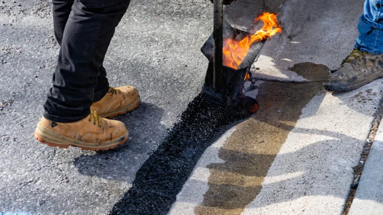 Close-up of a road worker using a flame and hot tarmac to repair a crack in a road surface.