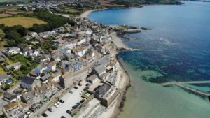 Aerial view of a coastal Cornish town showing dense housing and a large beachfront car park.
