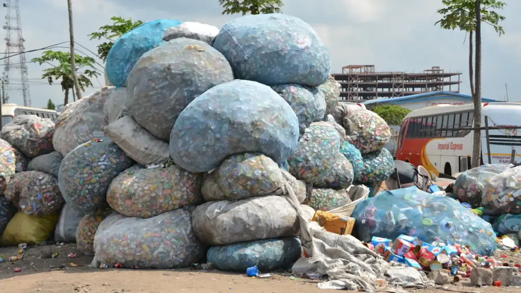 Large bags of recyclable plastic waste piled up near a city bus stop.
