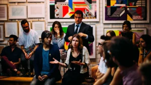 A diverse group of community members and a man in a business suit engage in a discussion at a local gallery.