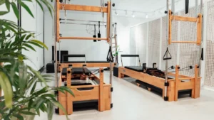 Wooden Reformer Pilates machines with black padding and metal frames in a bright fitness studio.