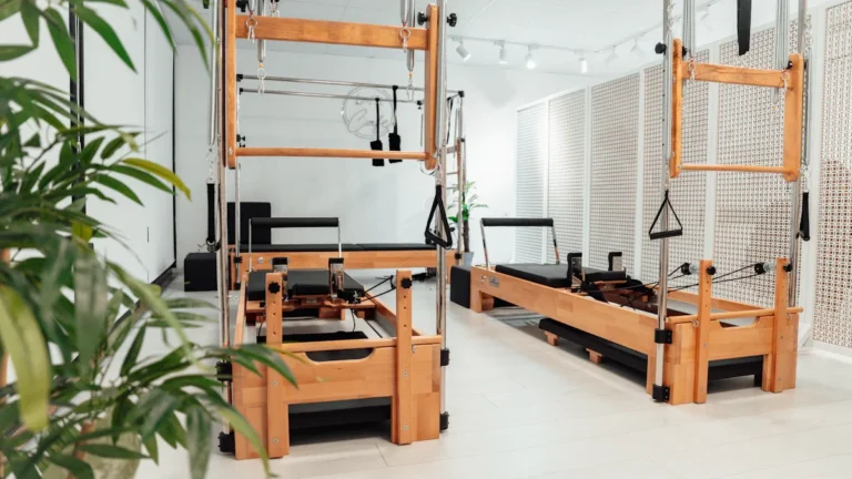 Wooden Reformer Pilates machines with black padding and metal frames in a bright fitness studio.
