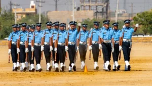 Military personnel in formation marching with rifles on a sunlit parade ground during a defense ceremony.