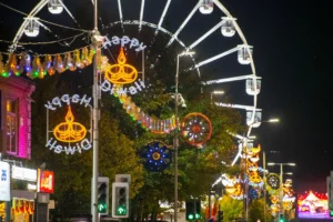 Illuminated Happy Diwali signs and a large Ferris wheel light up a festive city street.