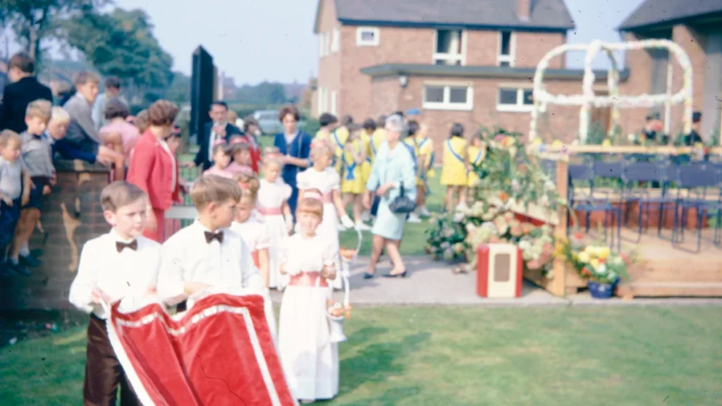 A vintage photograph of children in formal attire participating in an outdoor community parade in England.