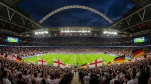 Fans waving England and Germany flags in a packed Wembley Stadium during a night football match.