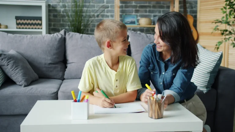 A boy and a woman smiling at each other while working together at a table, illustrating positive ADHD and autism support.