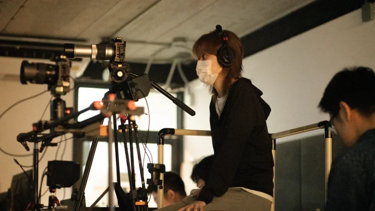 A young production intern wearing headphones and a mask operates professional film equipment.