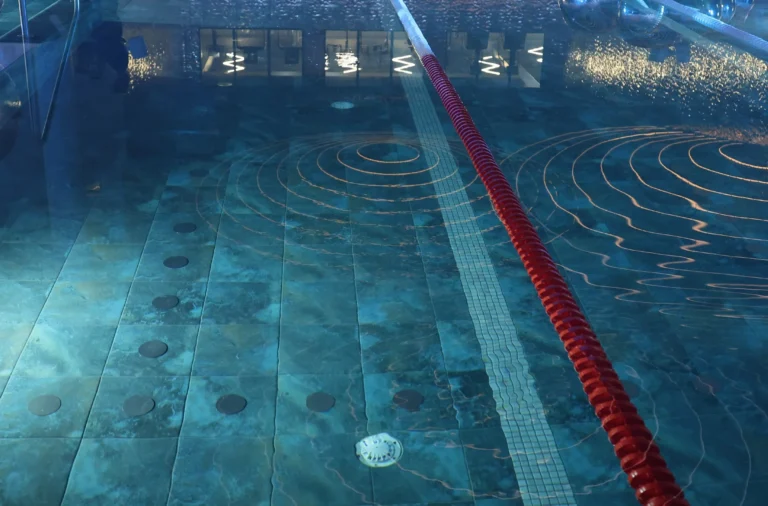 Indoor swimming pool featuring blue tiles, a red lane rope, and glowing orange circular light reflections.