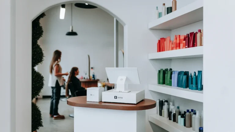 A modern beauty salon reception desk featuring a sleek payment terminal and shelves of professional products.