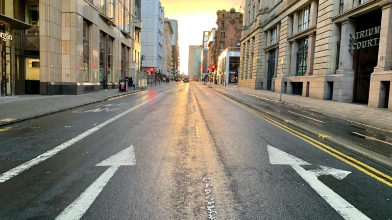 A wide-angle view of a major Glasgow city street with prominent white directional arrows on the asphalt, representing city road infrastructure.