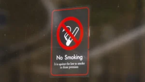 A no smoking sign on a glass window with text stating it is against the law to smoke on the premises.