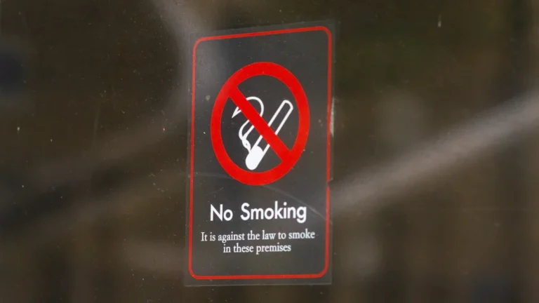 A no smoking sign on a glass window with text stating it is against the law to smoke on the premises.