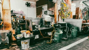 A cluttered and grimy commercial kitchen with visible grease and disorganized equipment.