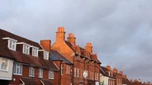 A row of traditional red brick houses with prominent chimneys under a cloudy sky in England.