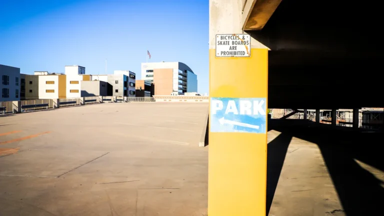A vacant rooftop level of a multi-story car park with a 'Park' sign on a yellow pillar.