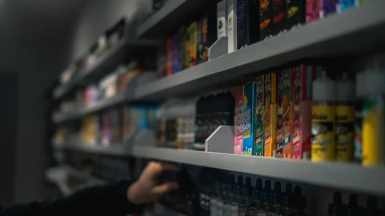 A person's hand reaching for a box of vape liquid on a shelf in a store.