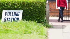A sign reading 'POLLING STATION' positioned on a grassy lawn next to a green hedge.