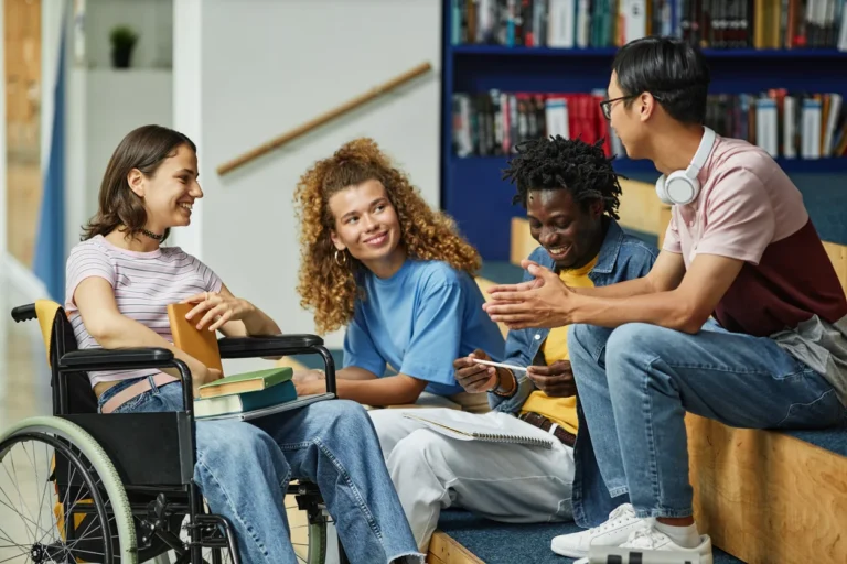 Diverse group of students, including a wheelchair user, talking and smiling in a modern library.