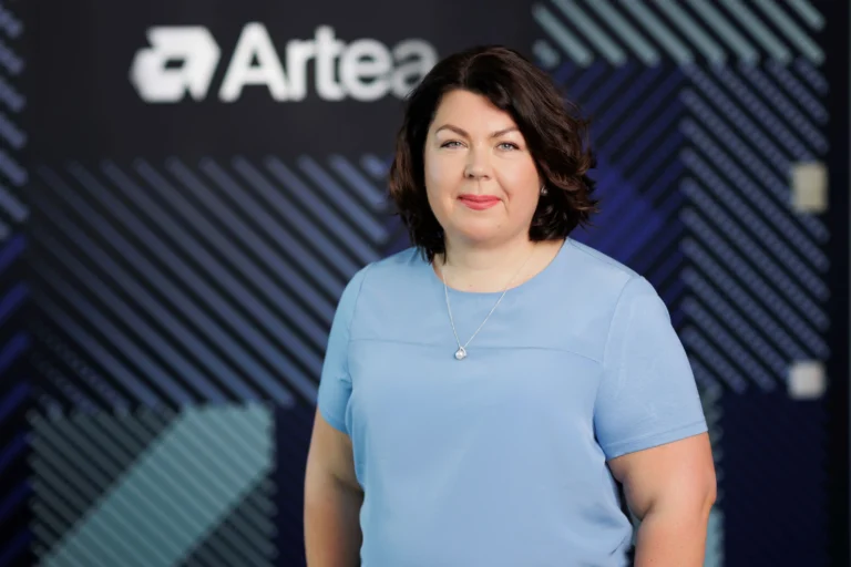 A dark-haired woman in a light blue top stands before a logo reading Artea.