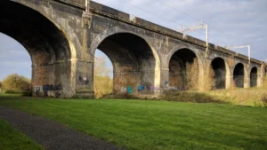 A large stone railway viaduct with tall arches crossing over a lush green field in the UK.