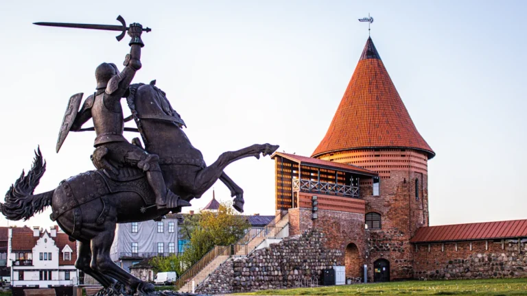 A majestic bronze statue of a medieval knight on horseback in front of Kaunas Castle.