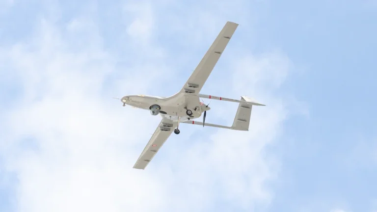 A military-grade fixed-wing surveillance drone flying against a bright, cloudy sky.