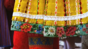 Close-up of traditional yellow folk clothing featuring colorful floral embroidery and white lace trim.