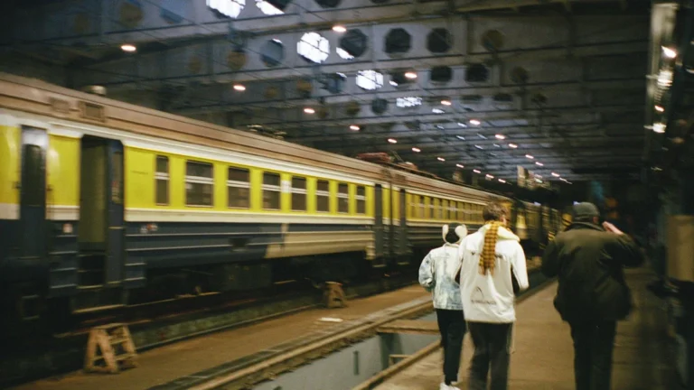 Passengers walking alongside a traditional yellow and blue passenger train at a rail station in Riga.