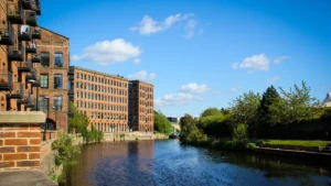 Large red brick industrial buildings converted into modern apartments along a river in Leeds.