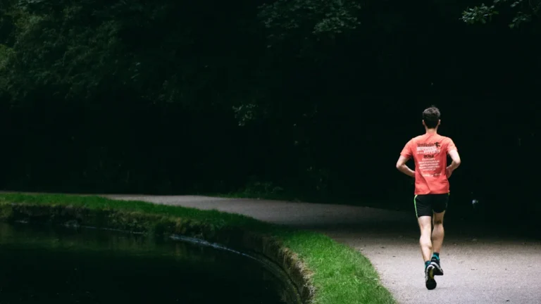 A runner in a bright orange shirt jogs along a peaceful canal path, signifying the training and preparation for the upcoming marathon.