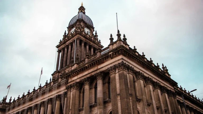 A dramatic low-angle view of the iconic Leeds Town Hall under an overcast sky, representing the seat of local government.